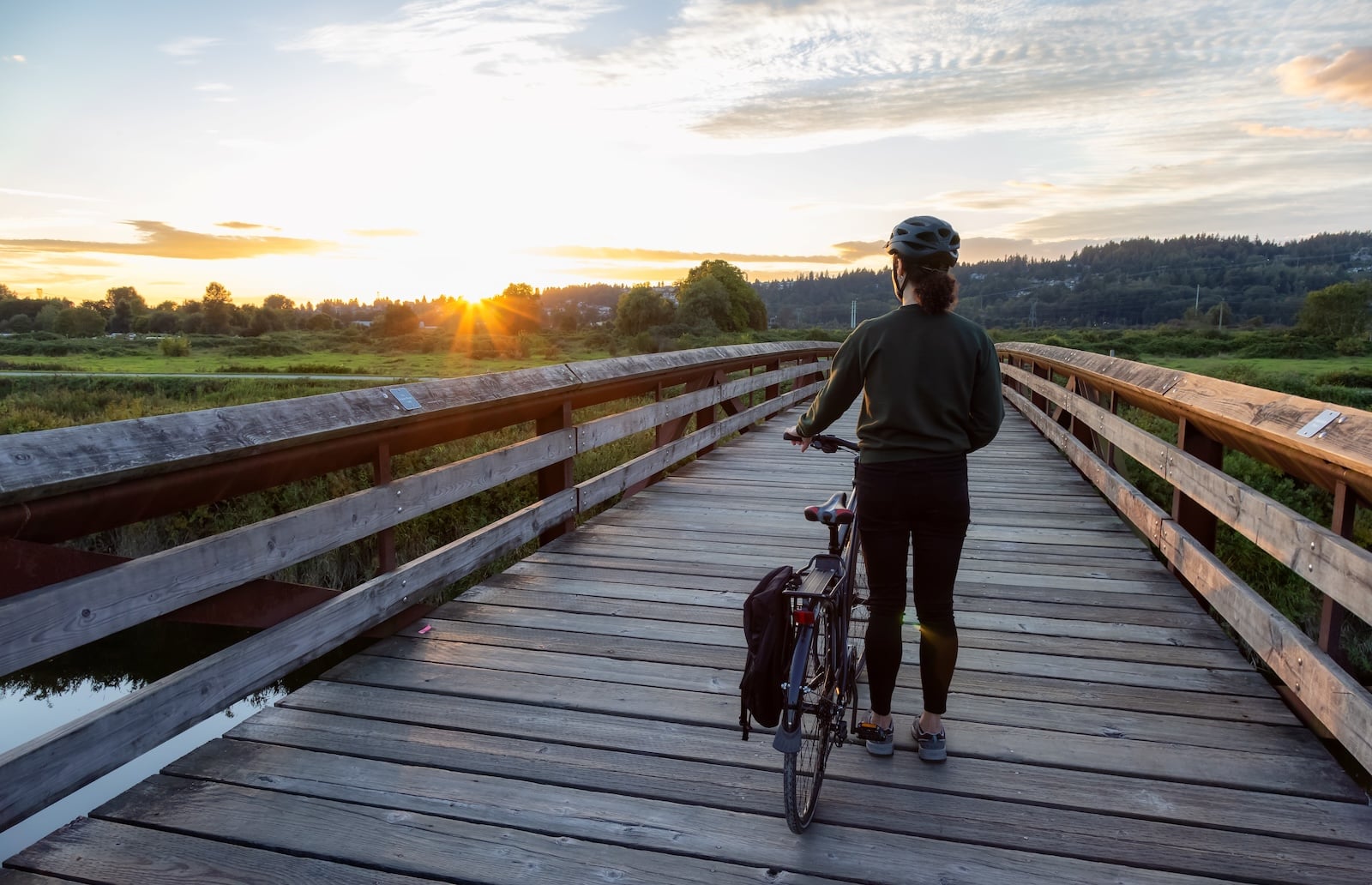 Woman riding a bike over a bride during sunset.